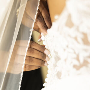 Close-up of a bride in a white lace wedding dress being buttoned up by a delicate hand highlighting bridal gown details and the intimate preparation on her wedding day.