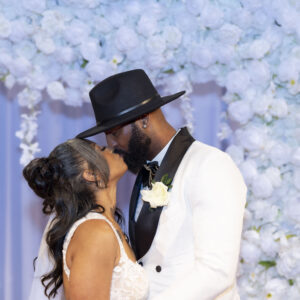Bride and groom sharing a romantic kiss in front of a beautiful white floral backdrop on their wedding day creating a memorable moment of love and joy.