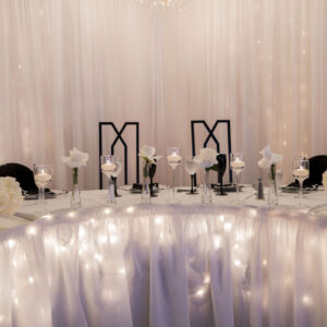 Elegant wedding table setting adorned with white flowers and warm candlelight against a backdrop of sheer drapes. Romantic ambiance for a special celebration.