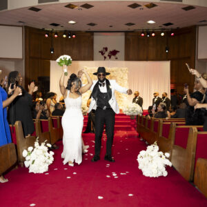 Bride and groom joyfully celebrate as they walk down the aisle in a beautifully decorated wedding venue filled with happy guests and elegant floral arrangements.