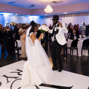 Bride and groom joyfully dancing at wedding reception in elegant venue with guests watching, featuring chic black and white decor and a chandelier-lit ballroom.
