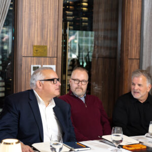 Business professionals seated at a formal dining table while a server takes orders in an upscale restaurant setting.