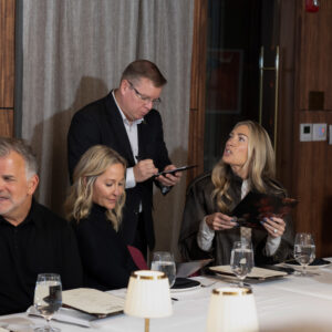 “Business professionals seated at a formal dining table while a server takes orders in an upscale restaurant setting.