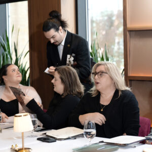 Corporate team attending a business presentation in a modern meeting room with a presenter speaking beside a screen