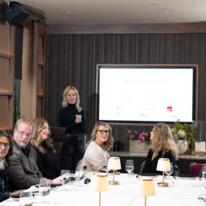 Corporate team attending a business presentation in a modern meeting room with a presenter speaking beside a screen