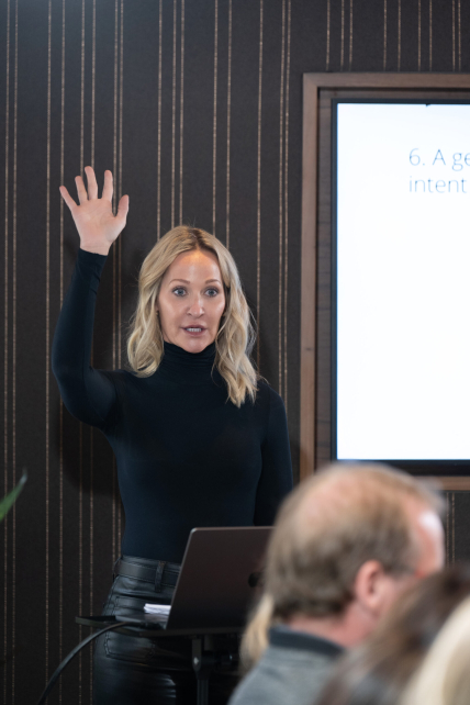Corporate presenter speaking confidently during a professional business meeting, wearing a black outfit and gesturing while addressing the team