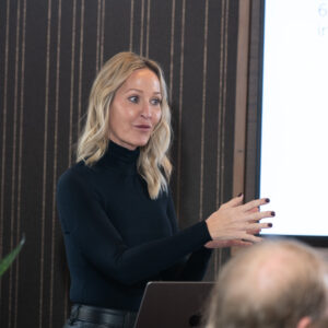 orporate presenter speaking confidently during a professional business meeting, wearing a black outfit and gesturing while addressing the team.