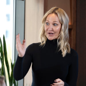 orporate presenter speaking confidently during a professional business meeting, wearing a black outfit and gesturing while addressing the team.