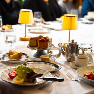 A beautifully set dining table with elegant tableware features fresh salads bread and beverages illuminated by warm yellow lamps creating an inviting atmosphere for guests.