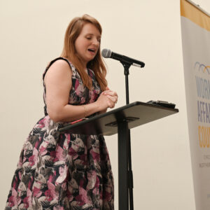 Woman speaking at a podium during a World Affairs Council event. She is wearing a floral dress and engaging with the audience on an important global topic.