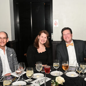 A group of people enjoying a formal dinner event at a restaurant with drinks and appetizers on the table creating a cheerful and elegant atmosphere.