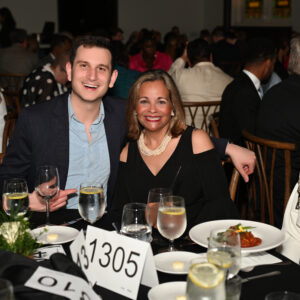 People enjoying a formal dinner event at a table covered with plates and wine glasses. A man and two women are sitting together smiling at the camera.