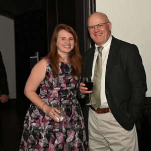 Man and woman smiling at an indoor event holding drinks dressed in formal attire creating a warm atmosphere with soft lighting and a sophisticated background.