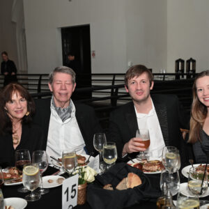 A group of four people enjoying a formal dinner at an elegant venue with plates of food and drinks on the table surrounded by a sophisticated atmosphere.
