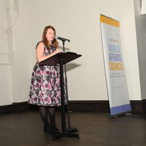 A woman in a floral dress speaks at a podium during a World Affairs Council event highlighting international relations and global discussions in a formal setting.