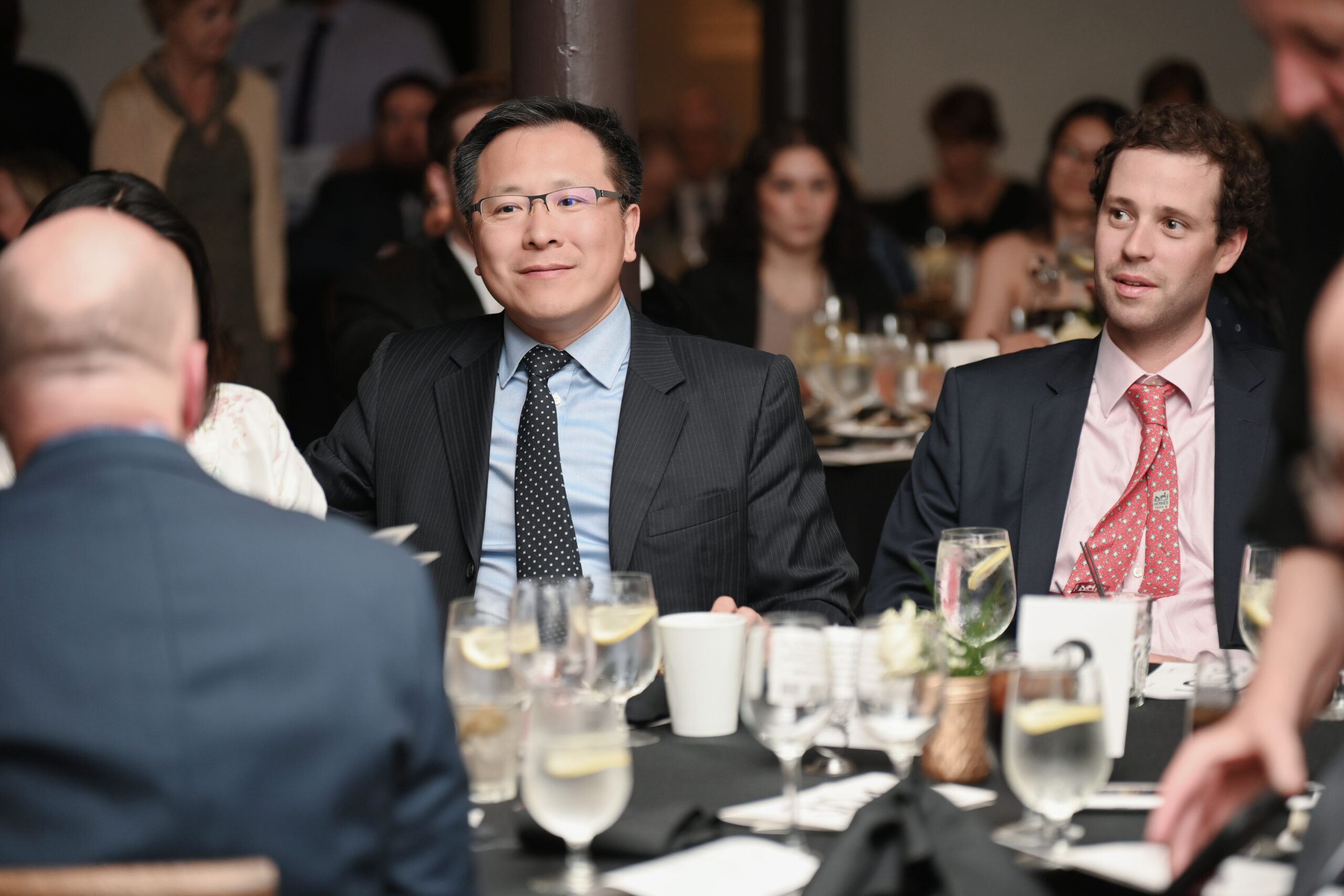 Business professionals attending formal dinner event with elegantly set tables and beverages, engaged in conversation, highlighting a networking and corporate atmosphere.