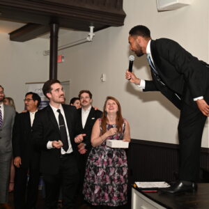 A man in a suit speaks passionately to an engaged audience at a formal event hosted by the World Affairs Council with attendees listening and interacting energetically.