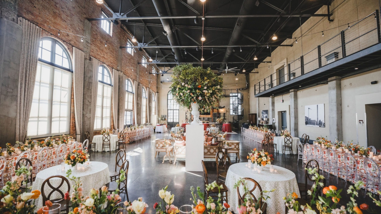Spacious industrial chic wedding venue with large windows and high ceilings decorated with elegant floral arrangements and beautifully set tables for a stylish celebration.
