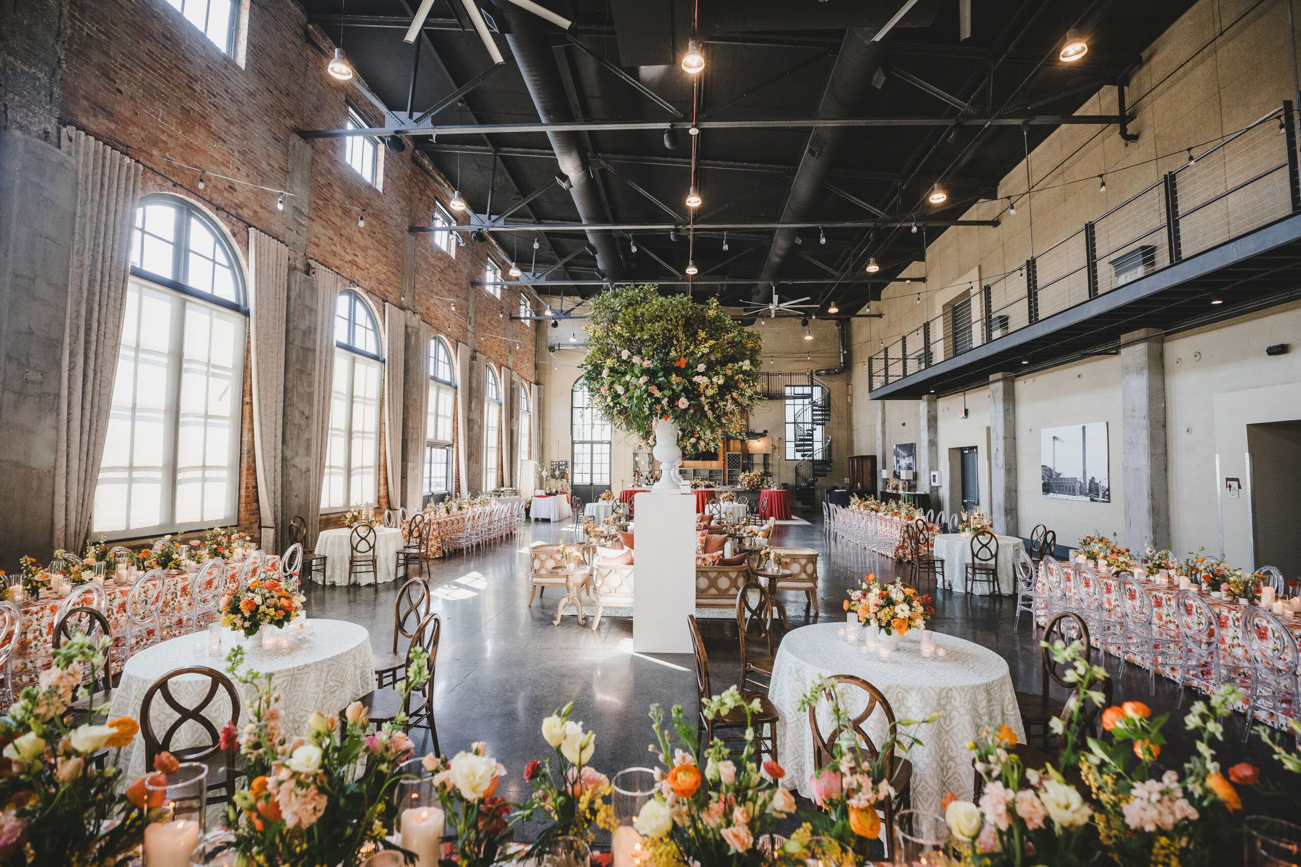 Spacious industrial chic wedding venue with large windows and high ceilings decorated with elegant floral arrangements and beautifully set tables for a stylish celebration.