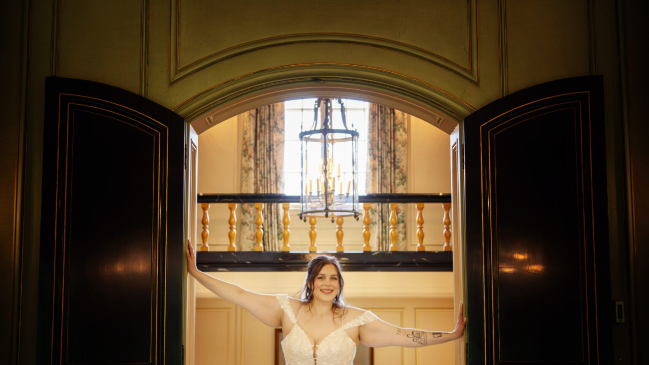 A bride in an elegant white gown poses in a grand entranceway under a sparkling chandelier offering a glimpse of a luxurious and stylish wedding setting. - wedding photo and video packages Ohio