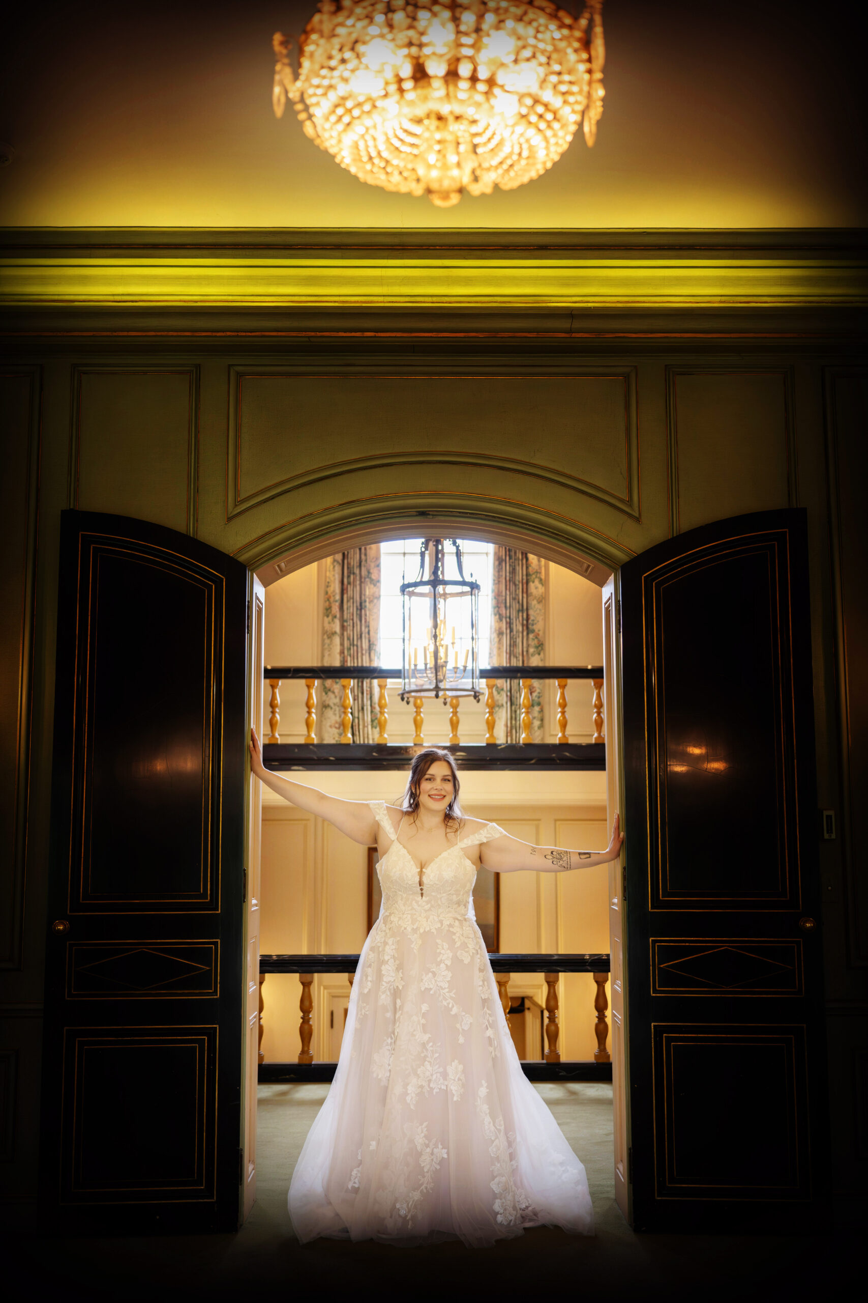 A bride in an elegant white gown poses in a grand entranceway under a sparkling chandelier offering a glimpse of a luxurious and stylish wedding setting. - wedding photo and video packages Ohio