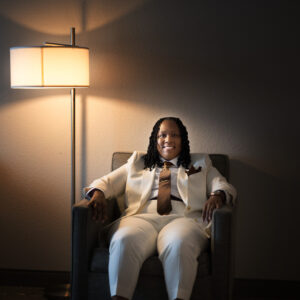A person in a white suit sits confidently in an armchair, illuminated by a warm floor lamp, creating a calm and professional atmosphere in the dimly lit room.