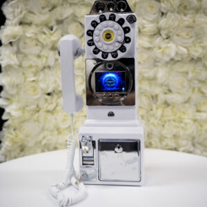 Vintage white rotary payphone with a modern twist featuring a blue lit screen set against a backdrop of elegant white roses on a smooth white surface.