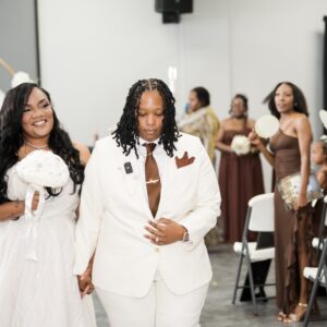 A newlywed couple happily walking hand in hand during their wedding ceremony, surrounded by friends and family dressed in elegant attire, celebrating their special day.