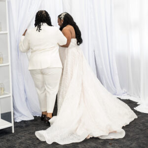 A joyful couple in elegant wedding attire stands together facing white curtains creating a beautiful and intimate wedding scene filled with love and elegance.