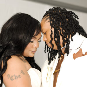 An LGBTQ+ bride and groom share a quiet forehead-to-forehead embrace before their wedding ceremony, dressed in elegant white wedding attire during an intimate portrait.