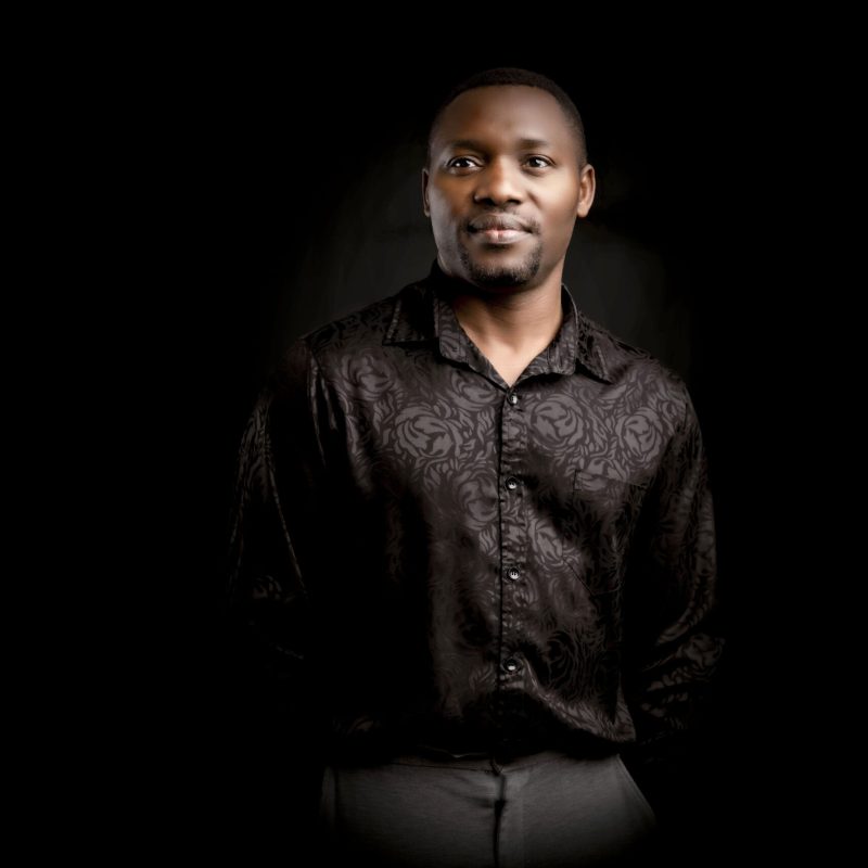Portrait of a man in a dark textured shirt against a black background looking confidently at the camera representing strength and sophistication in a professional setting